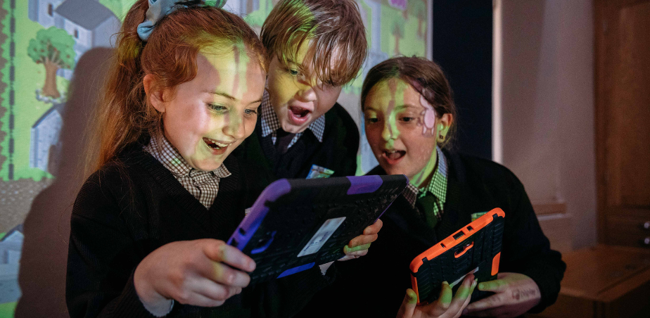 Two schoolchildren look at a tablet held by a third school child