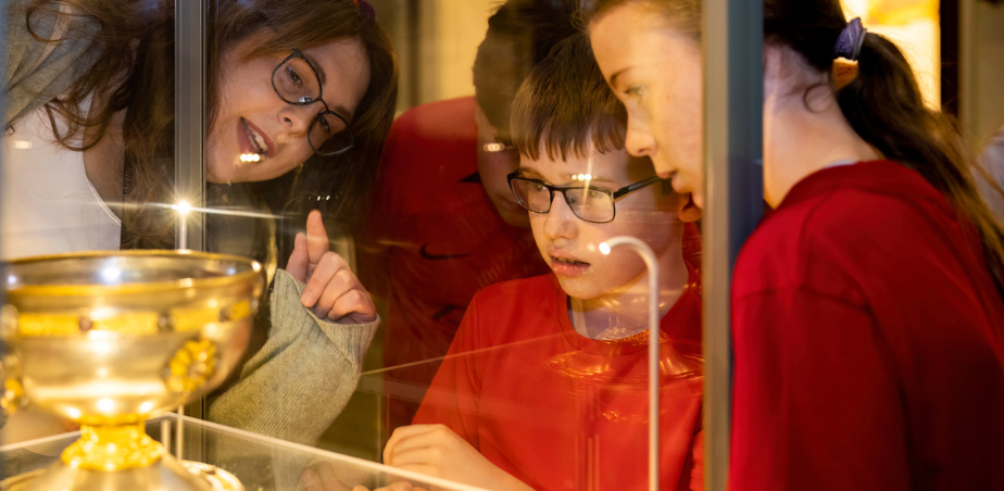 A group of school children in red polo shirts viewing a Viking artefact through the glass of a vetrine. An adult is pointing at the artefact.