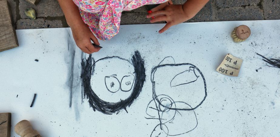 Close up of a child drawing a portrait on a sheet of paper laid on cement