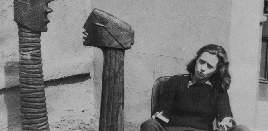 Sculptor Hilary Heron sitting in an outdoor location adjacent to two upright sculpture works