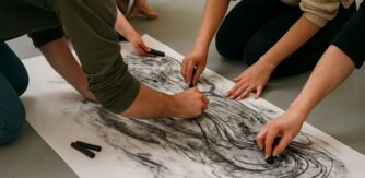 Students from MA in Arts and Engagement at Crawford College of Art draw on a large piece of paper on the ground.