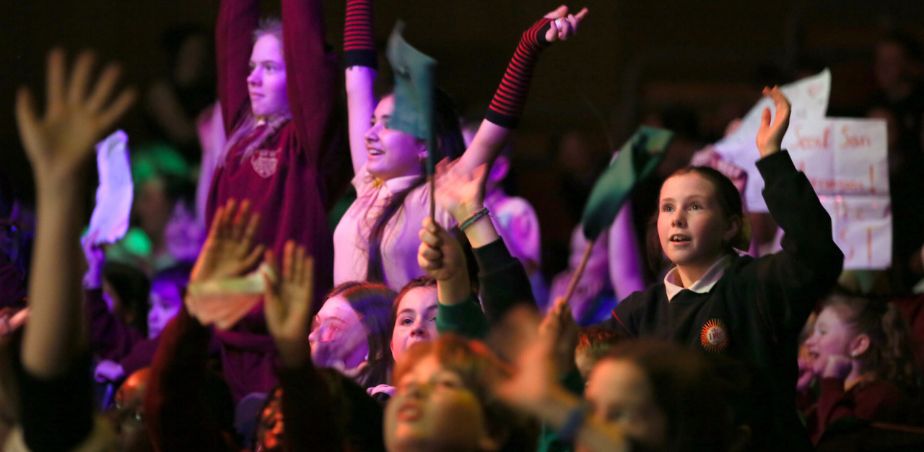 An audience of young people with raised hands and banners at a film awards event