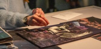 A TY students hand hovers over a collage of images on black paper. VISUAL Collective TY Programme