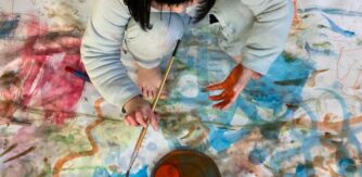 A child paints on a large white cloth covered in colourful swirls